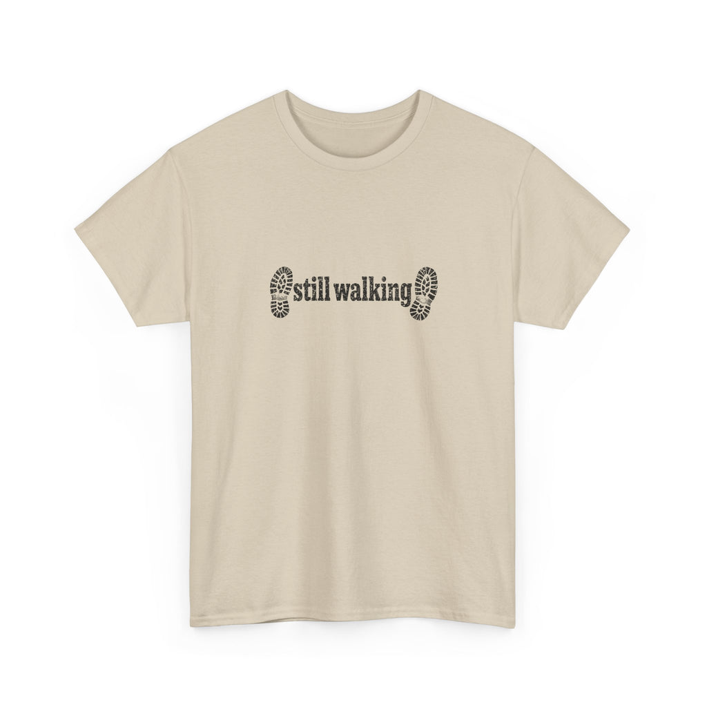 Beige t-shirt with 'still walking' text and footprints on a white background
