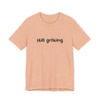 Beige t-shirt with 'still growing' text on a white background